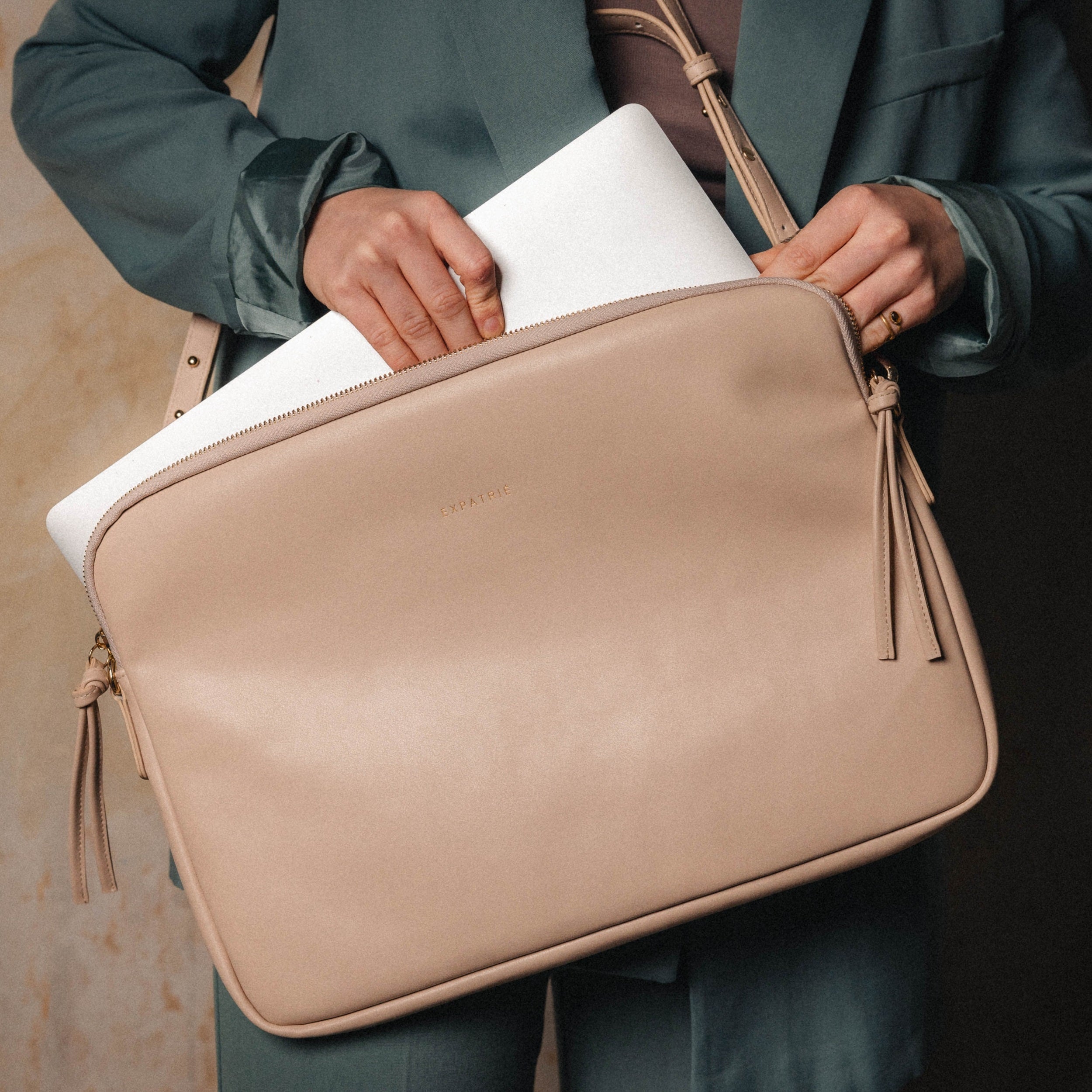 Beige Laptop Tasche Marlene aus Leder mit Reißverschluss, gehalten von Person in grünem Blazer