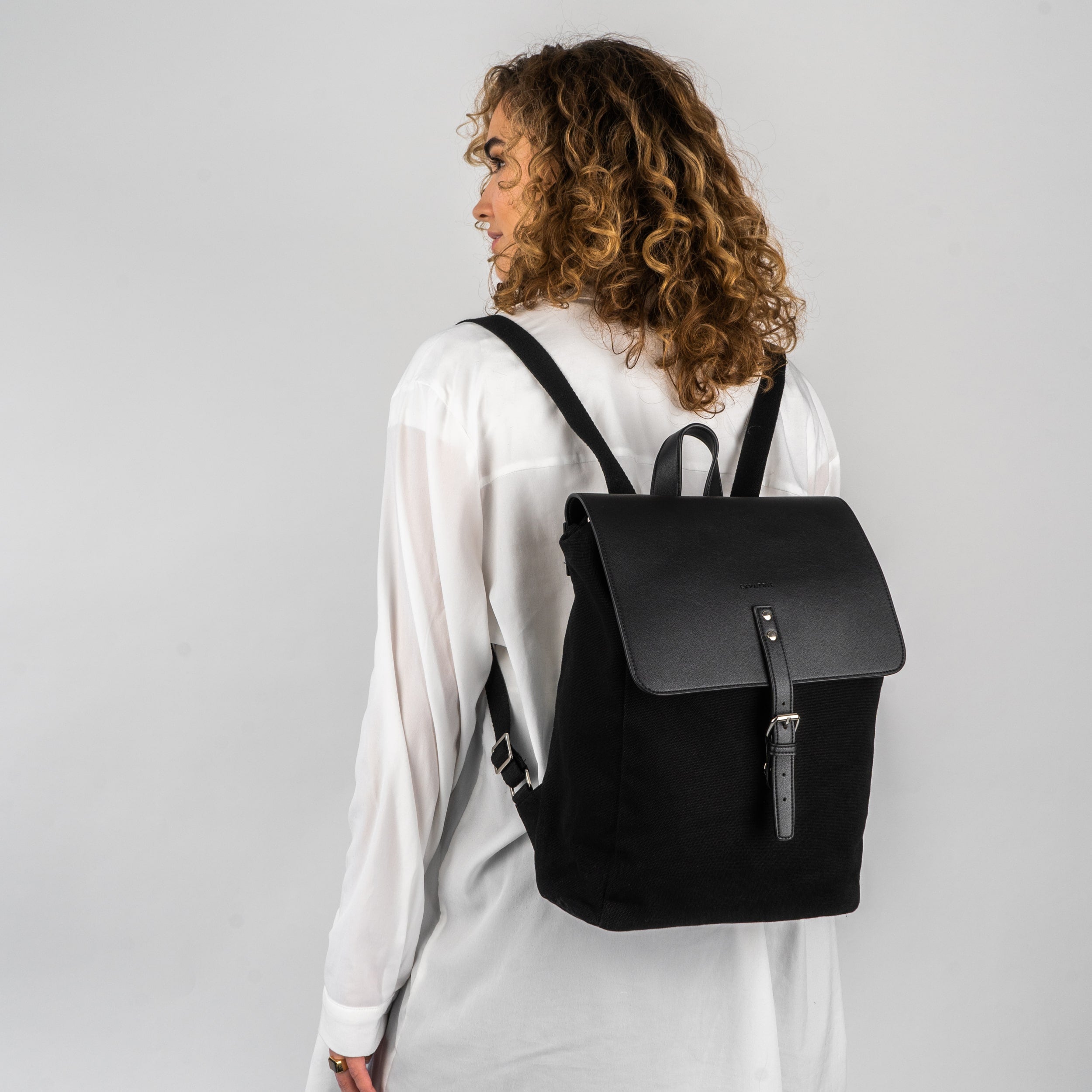 Frau mit lockigem Haar trägt schwarzen Canvas-Leder Rucksack 'Anouk' mit Schnallenverschluss