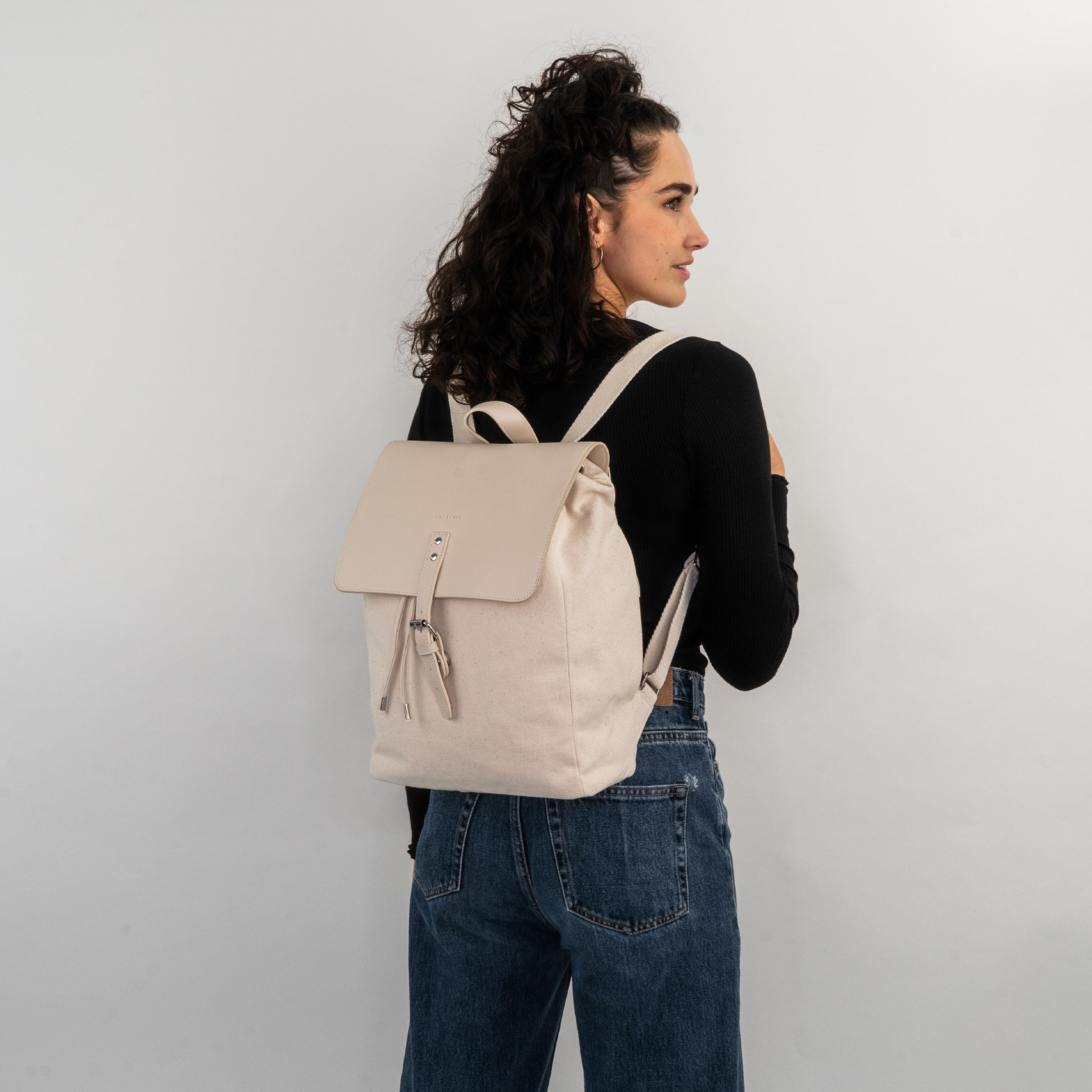 Beige-weißer Canvas-Leder-Rucksack 'Anouk' an einer Frau mit schwarzem Oberteil und Jeans