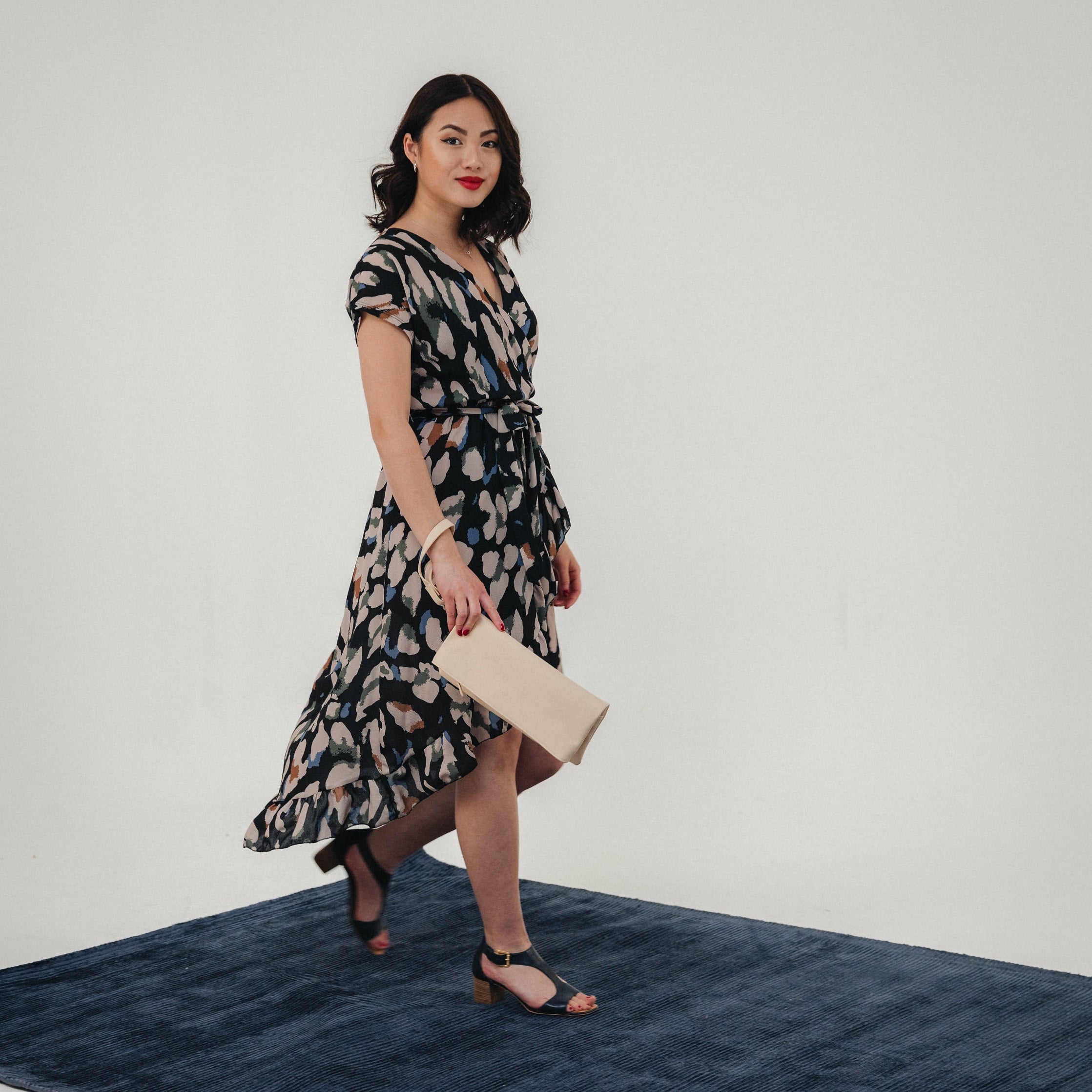 Frau in gemustertem Midikleid und schwarzen Sandalen mit beiger Leder-Clutch 'Marie' in der Hand