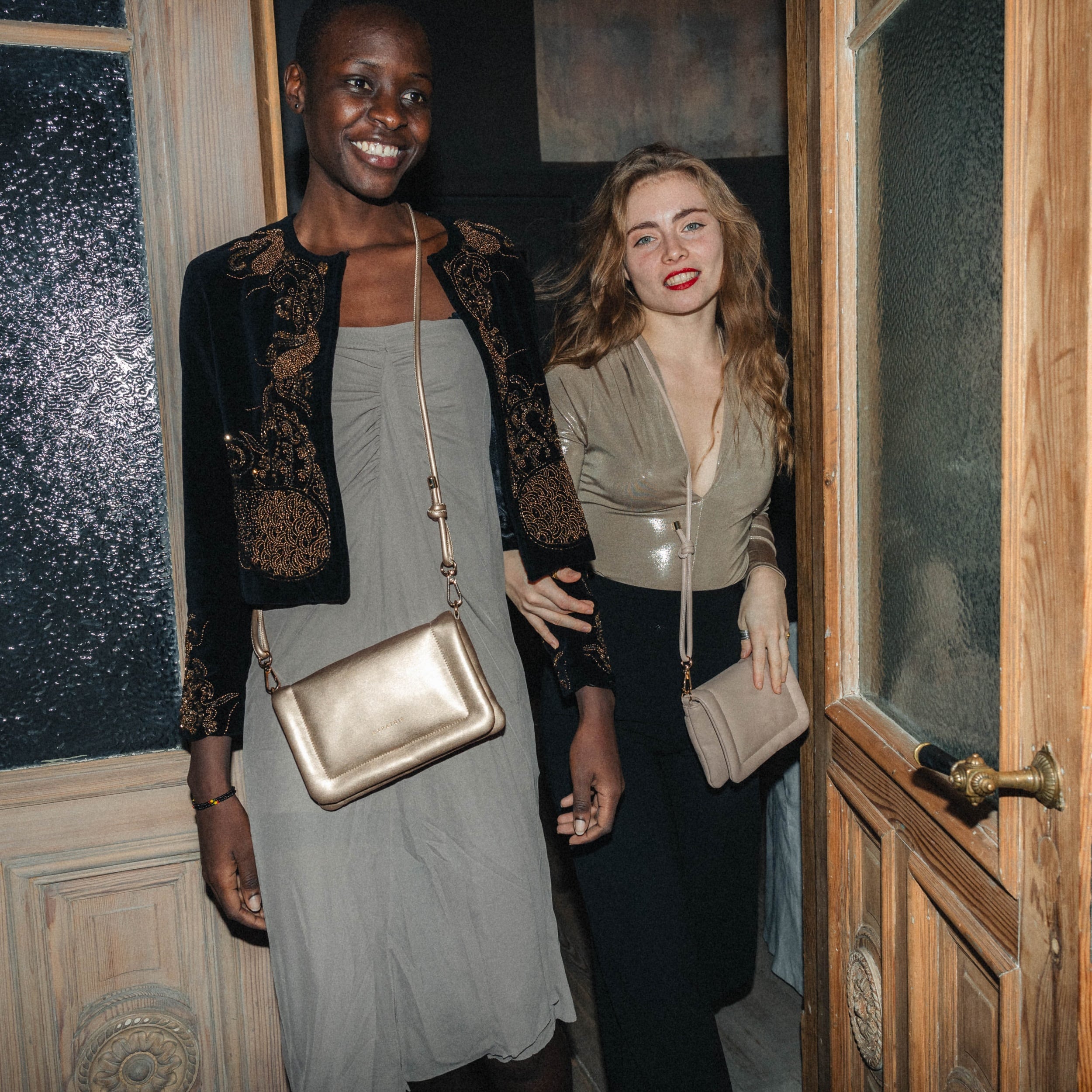 Zwei Frauen tragen Umhängetaschen Zoe Small in Gold und Beige bei Nacht