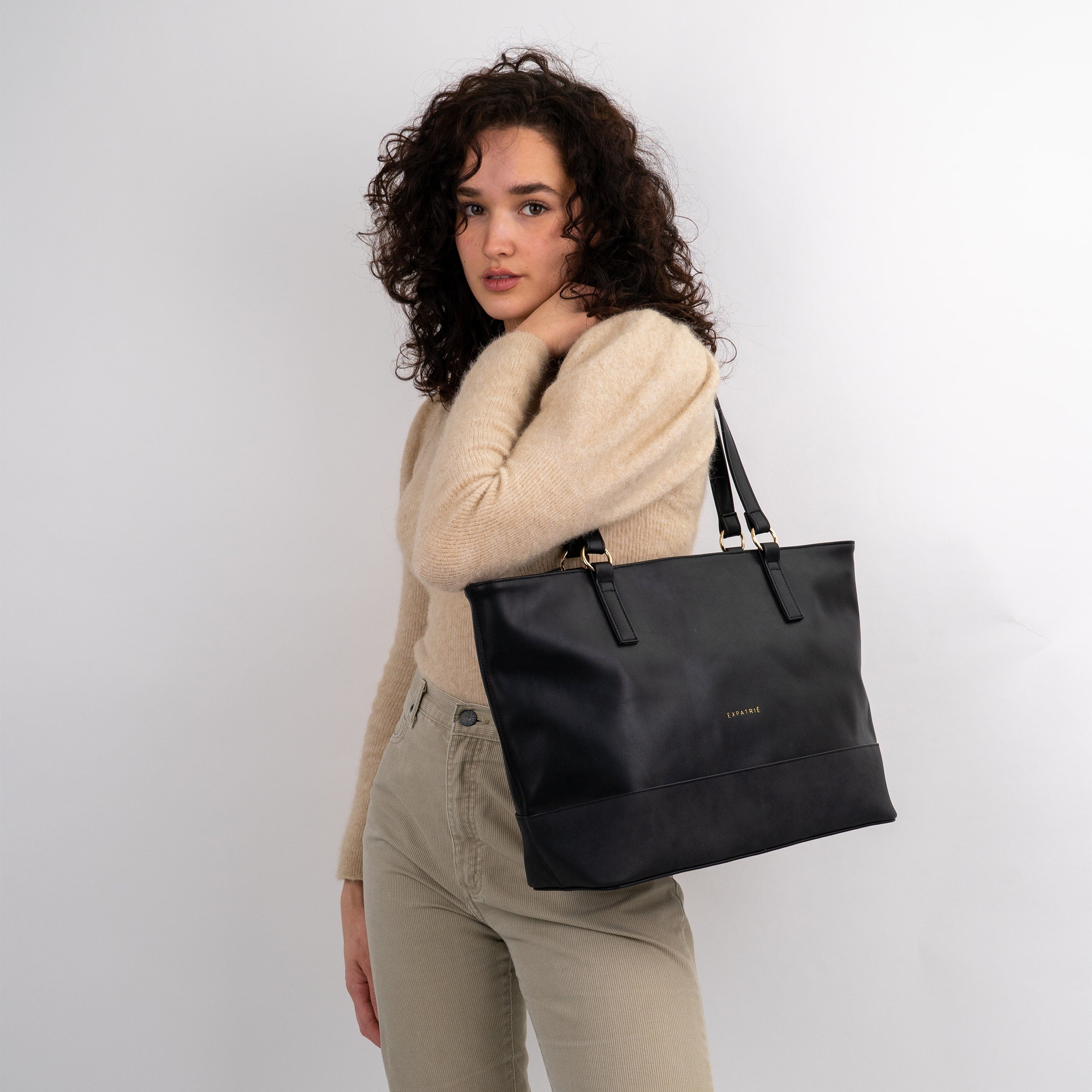 Frau mit lockigen Haaren trägt schwarze Shopper Tasche 'Nicole' von Expatrié über der Schulter