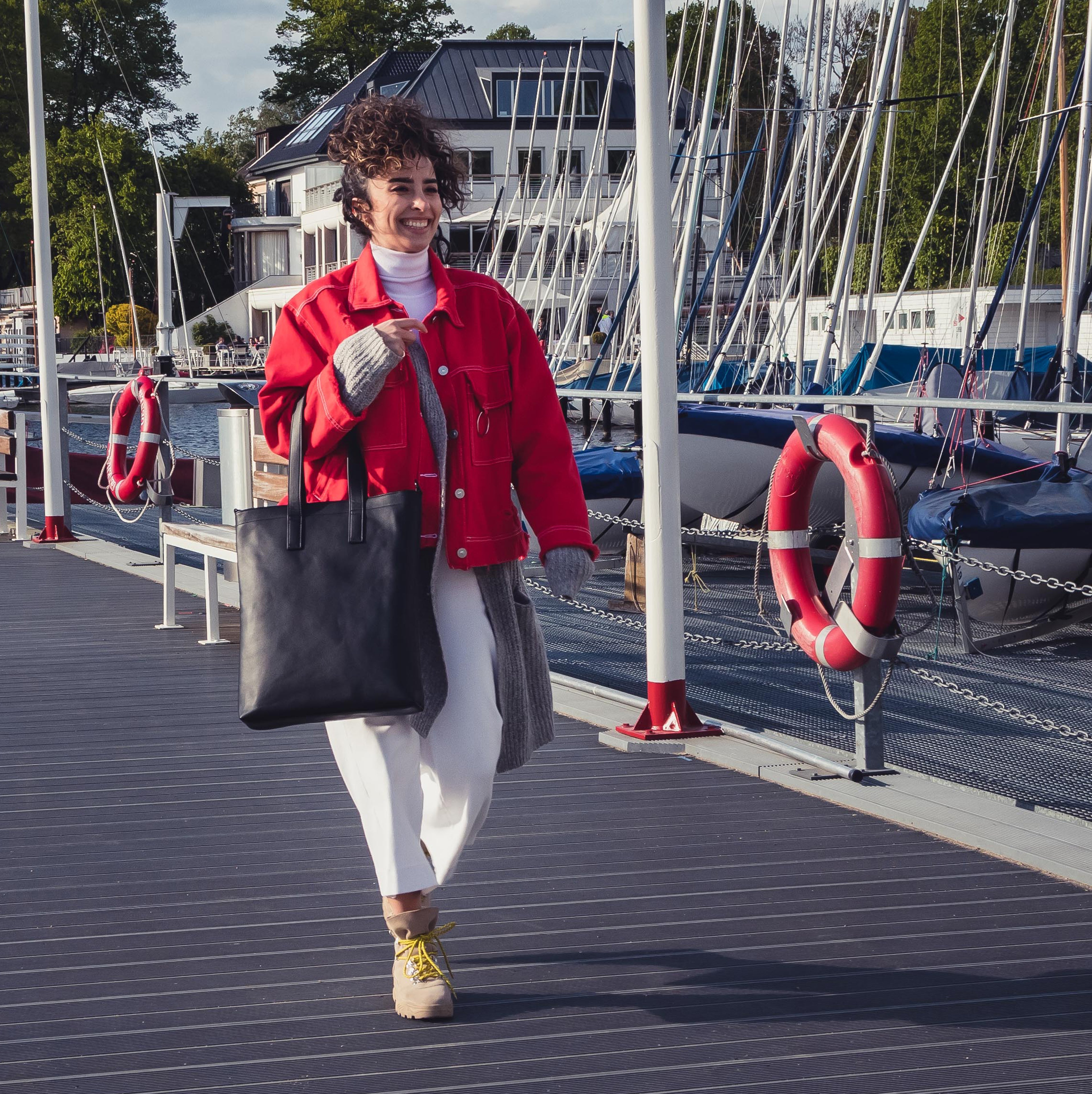 Frau trägt schwarze Ledertasche Sophie in rechteckiger Form am Steg neben Segelbooten