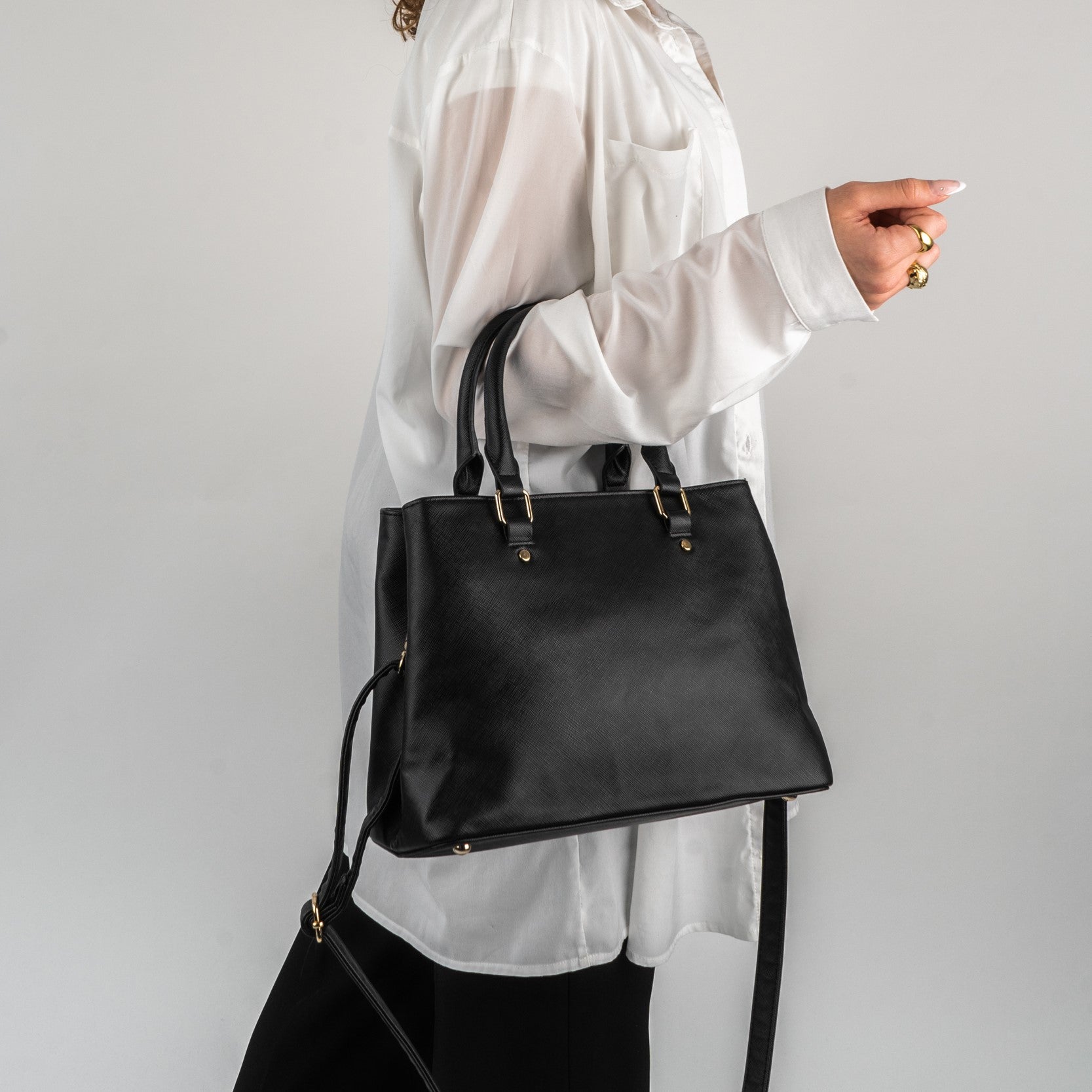 Schwarze Henkeltasche Julie aus strukturiertem Material, getragen von Frau in weißer Bluse