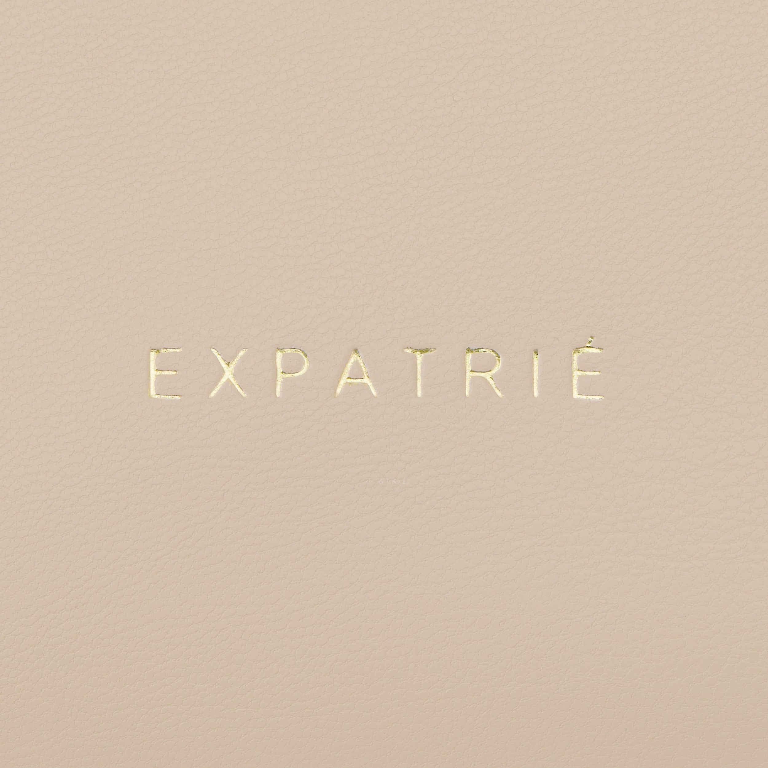 Goldener Schriftzug 'EXPATRIÉ' auf beige gepolstertem Kunstleder der Umhängetasche Zoe Medium