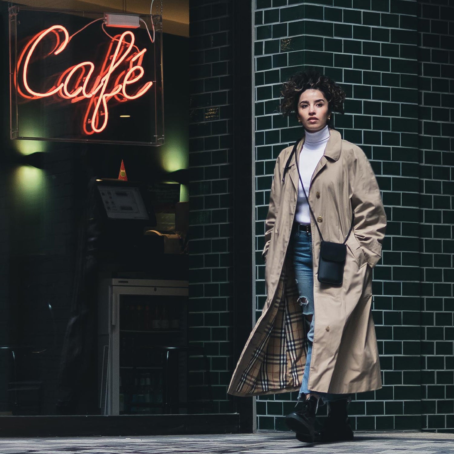 Frau trägt beige Trenchcoat, weiße Rollkragenpullover, Blue Jeans und schwarze Handy-Umhängetasche Amelie