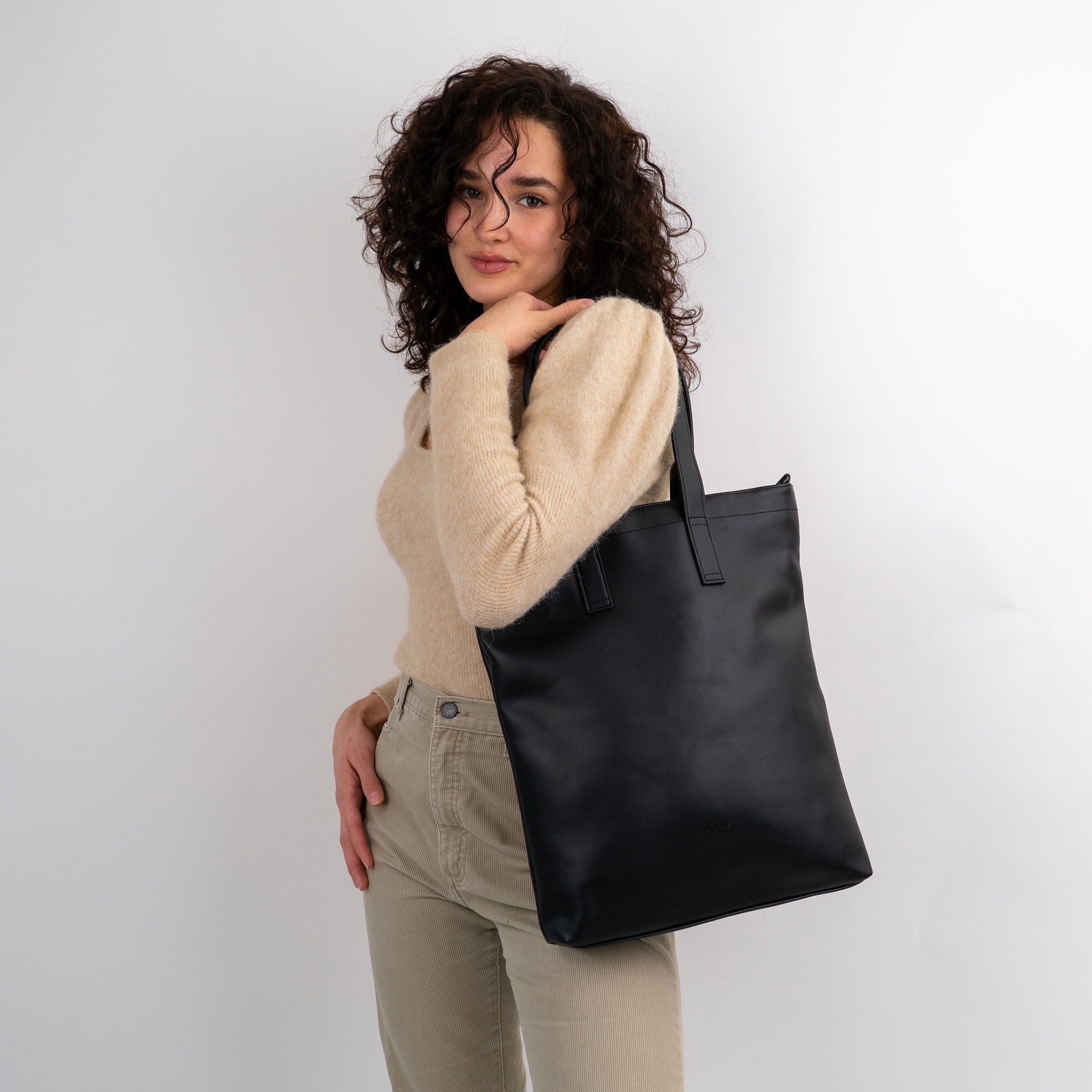 Frau mit dunklen lockigen Haaren trägt schwarze Business-Laptoptasche Handtasche Sophie