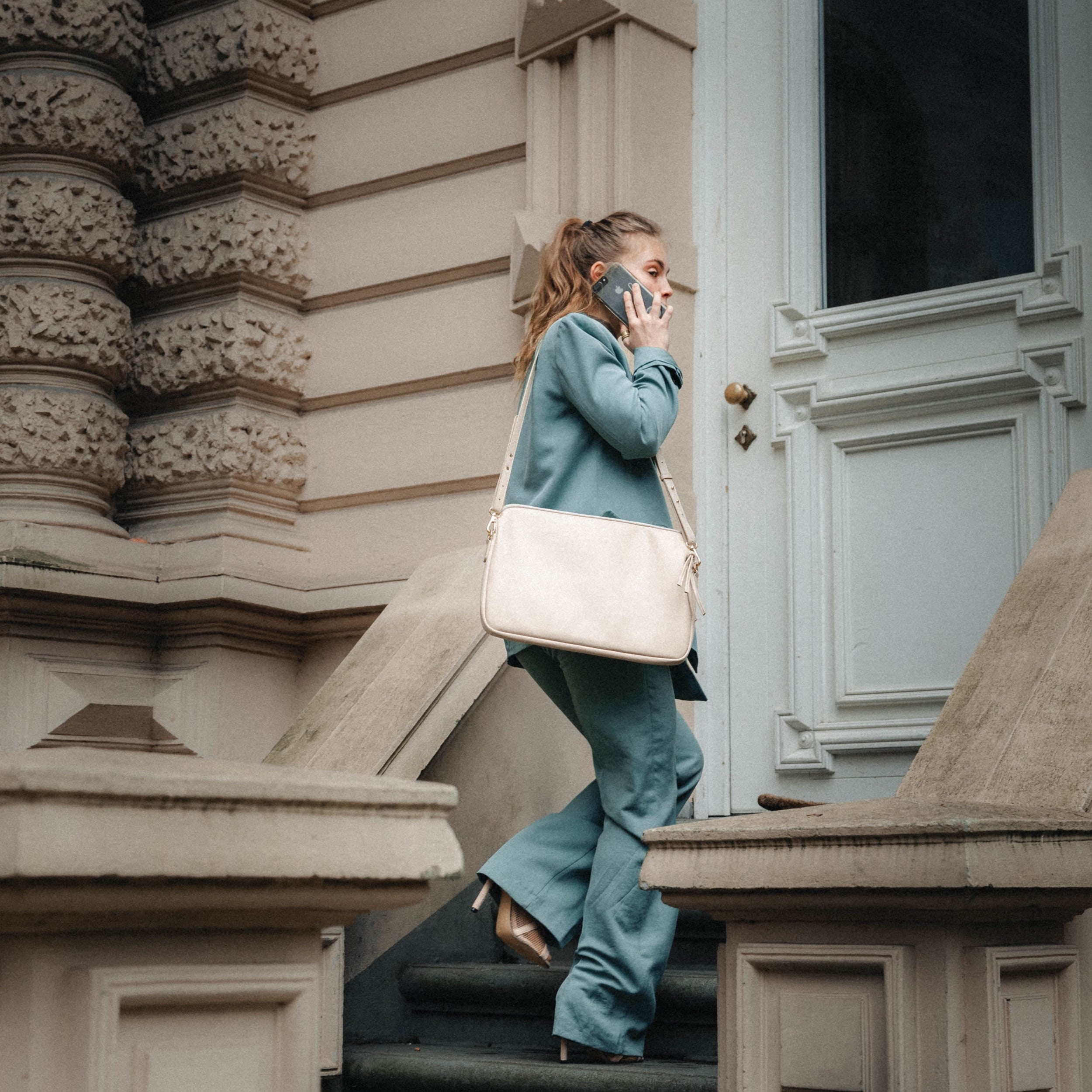 Frau in blauem Anzug trägt beige Laptop Tasche Marlene und telefoniert beim Treppenaufgang