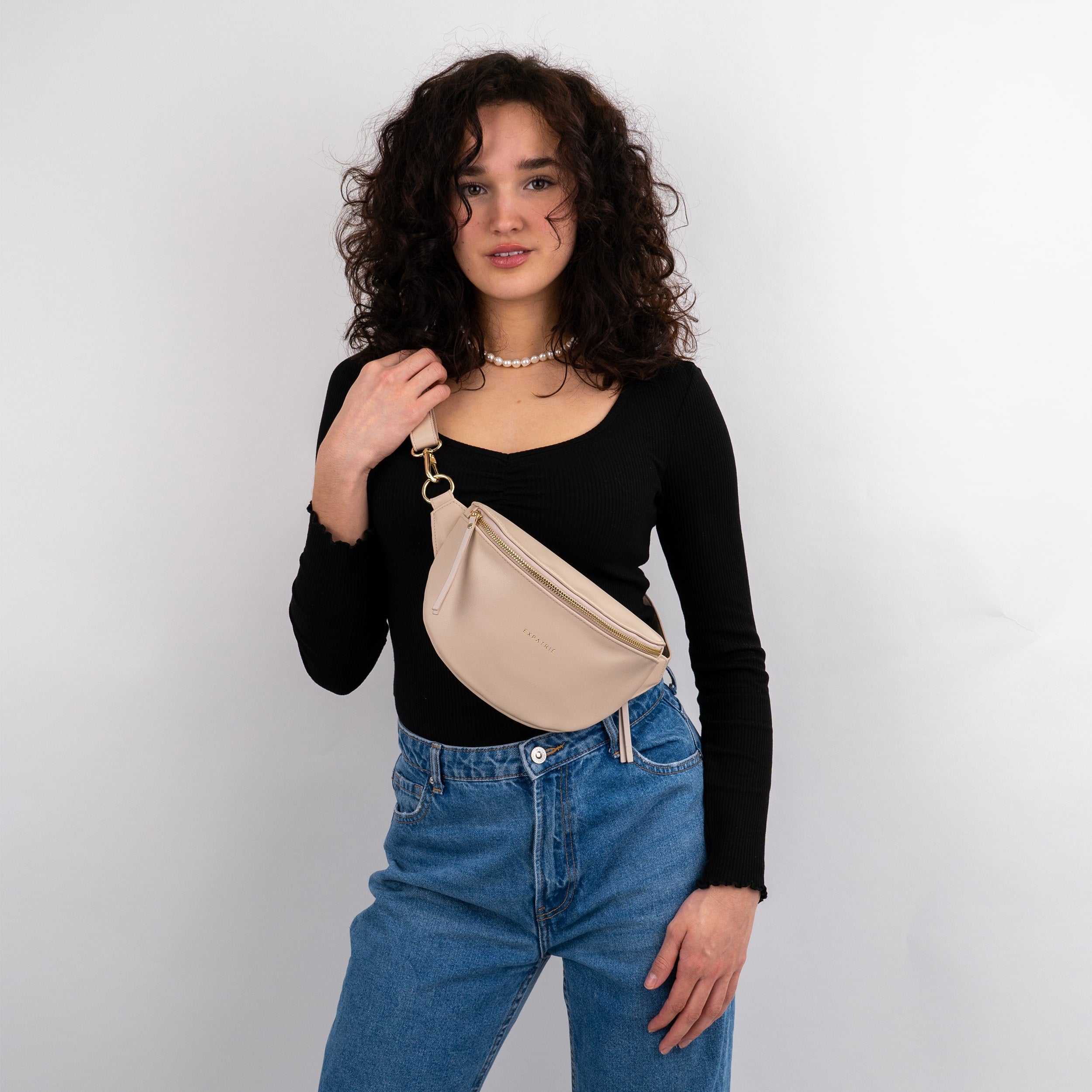 Frau trägt beige Leder-Bauchtasche Alice Small über schwarzen Oberteil und blauen Jeans