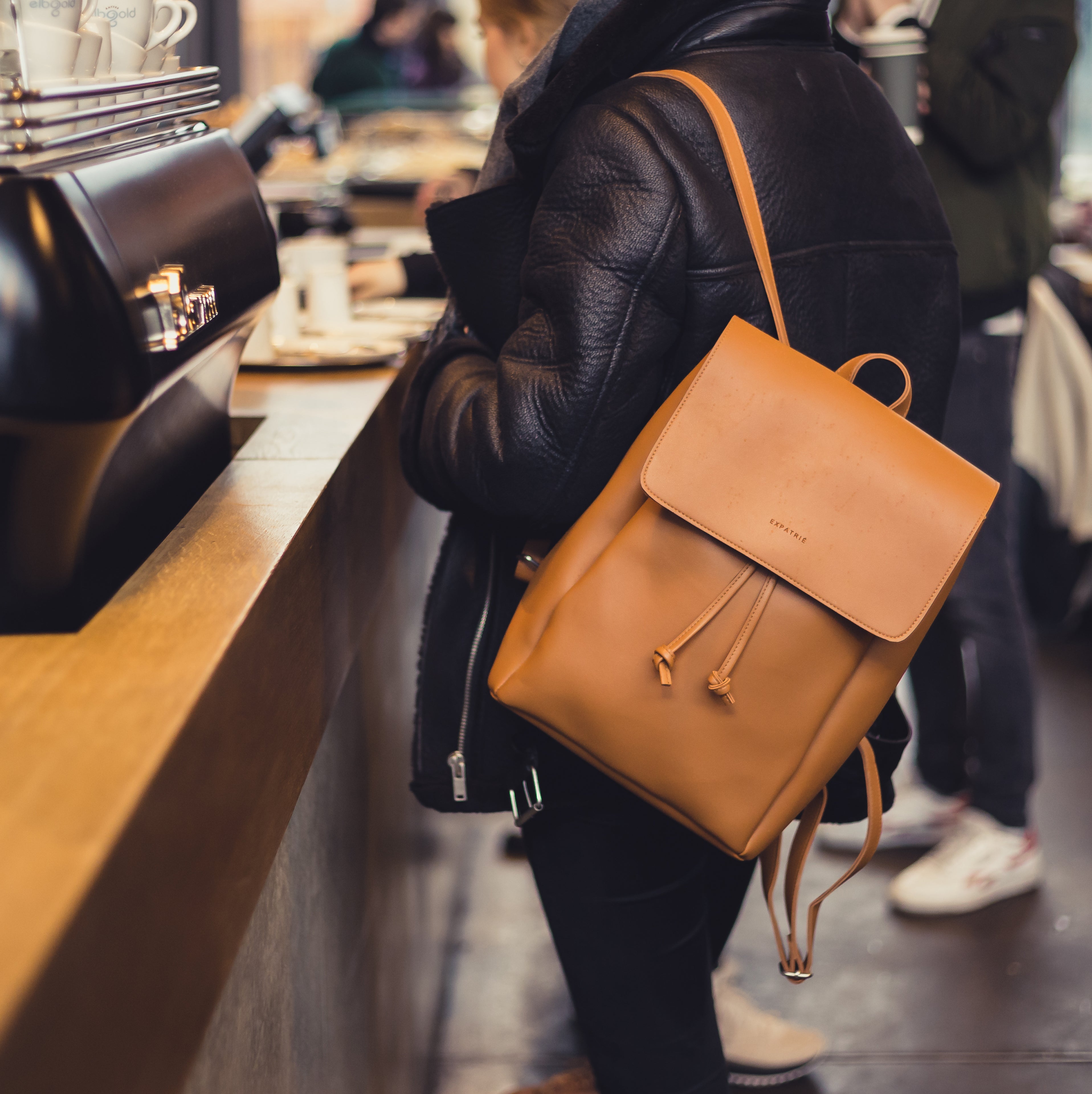 Kunstleder Rucksack Noelle in braun an Frau mit schwarzer Jacke in Café