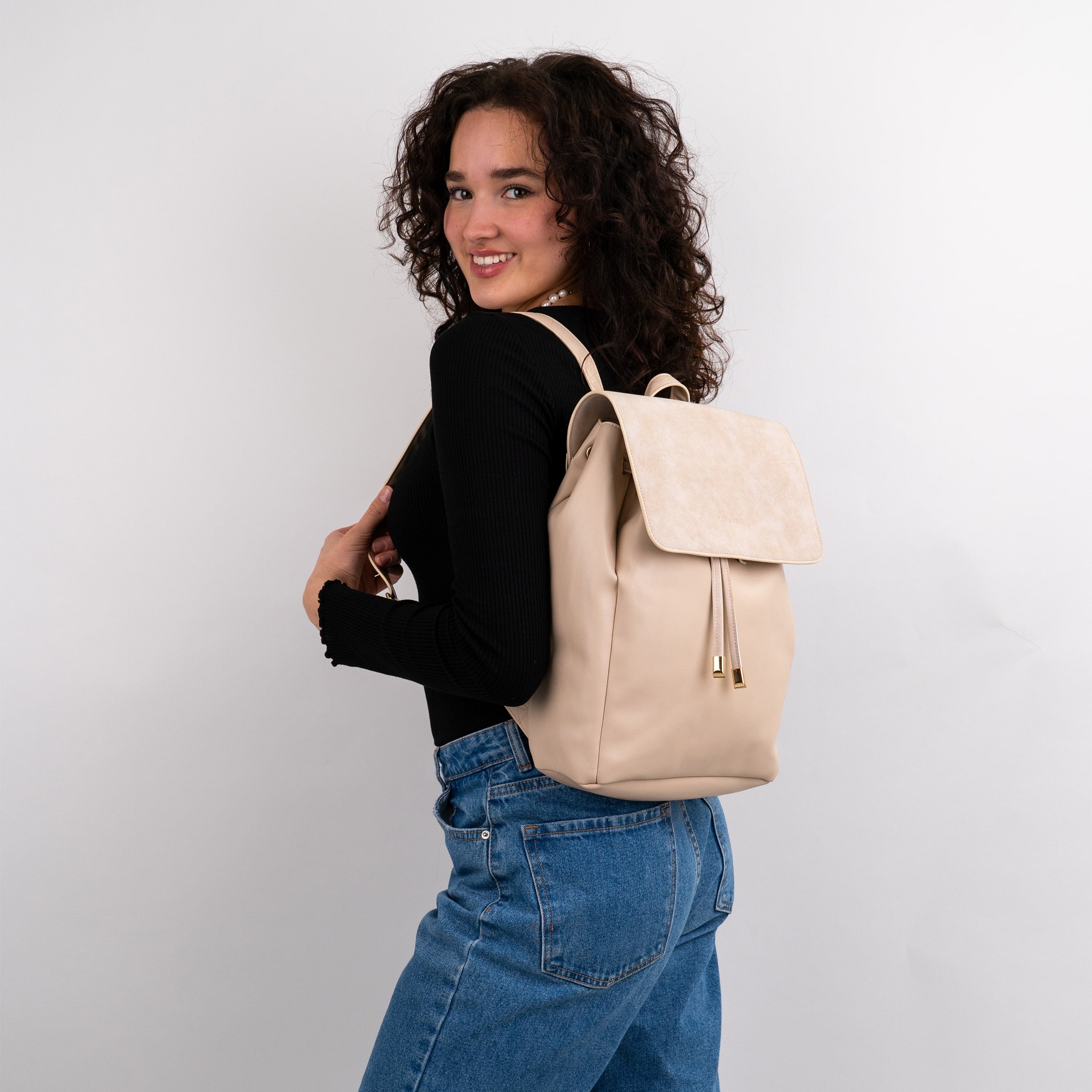 Beiger Kunstleder Rucksack Estelle an Frau mit schwarzem Oberteil und blauer Jeans