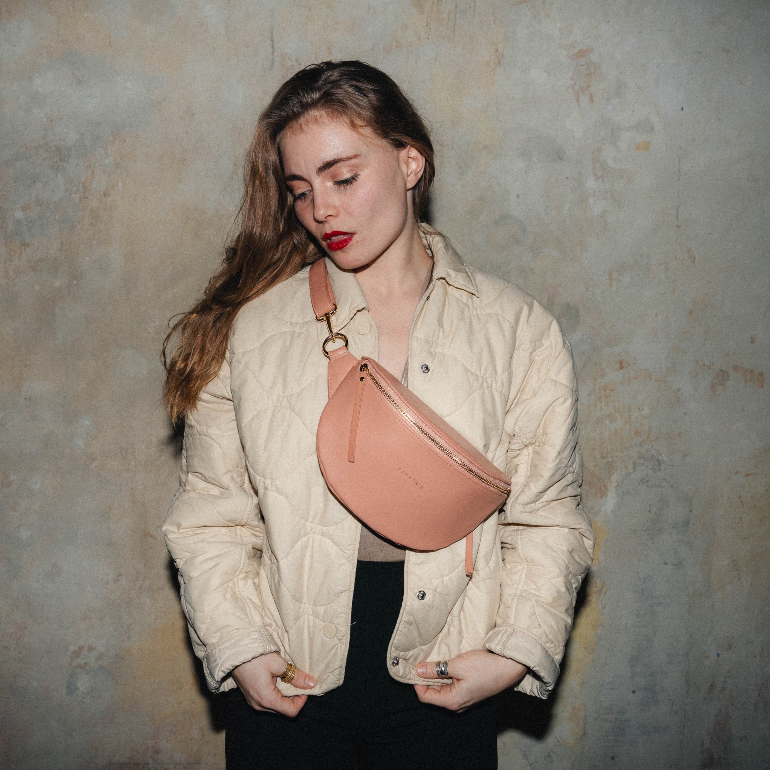 Frau mit rotem Lippenstift trägt eine hellbraune Bauchtasche Alice Small über einer cremefarbenen Steppjacke