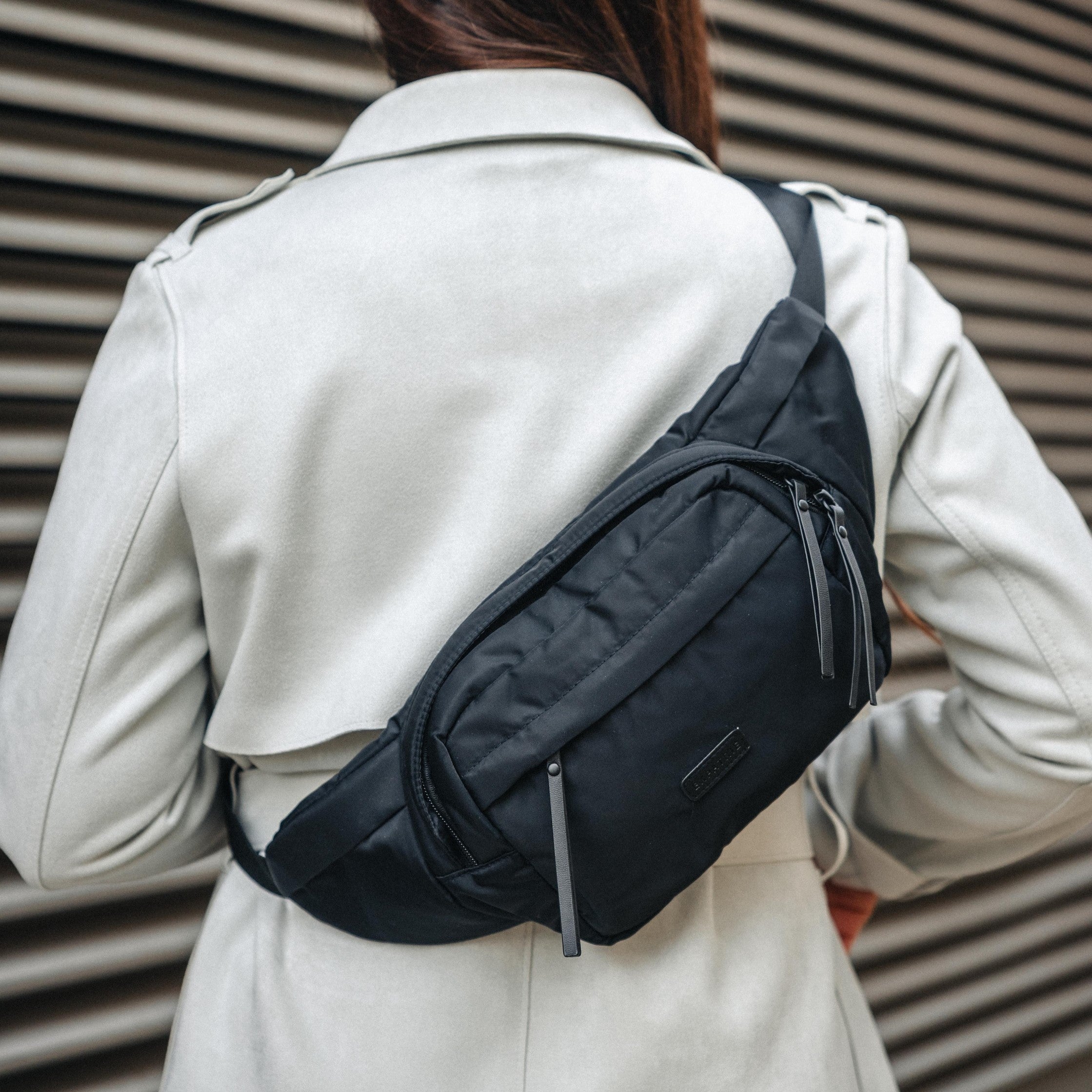 Schwarze Bauchtasche Justine aus Nylon mit mehreren Reißverschlusstaschen, getragen über dem Rücken