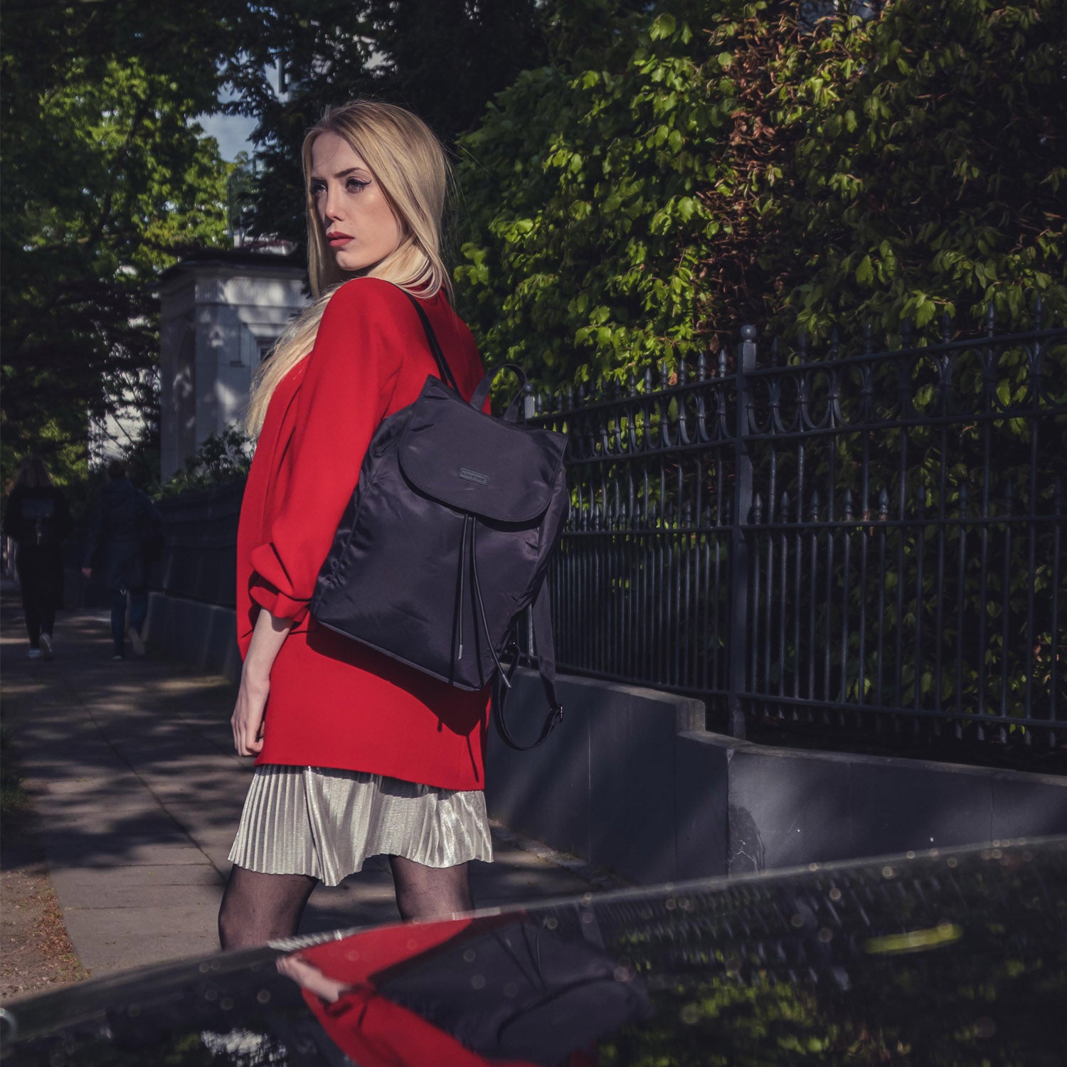 Frau im roten Blazer trägt schwarzen Nylon Rucksack Clara im Freien