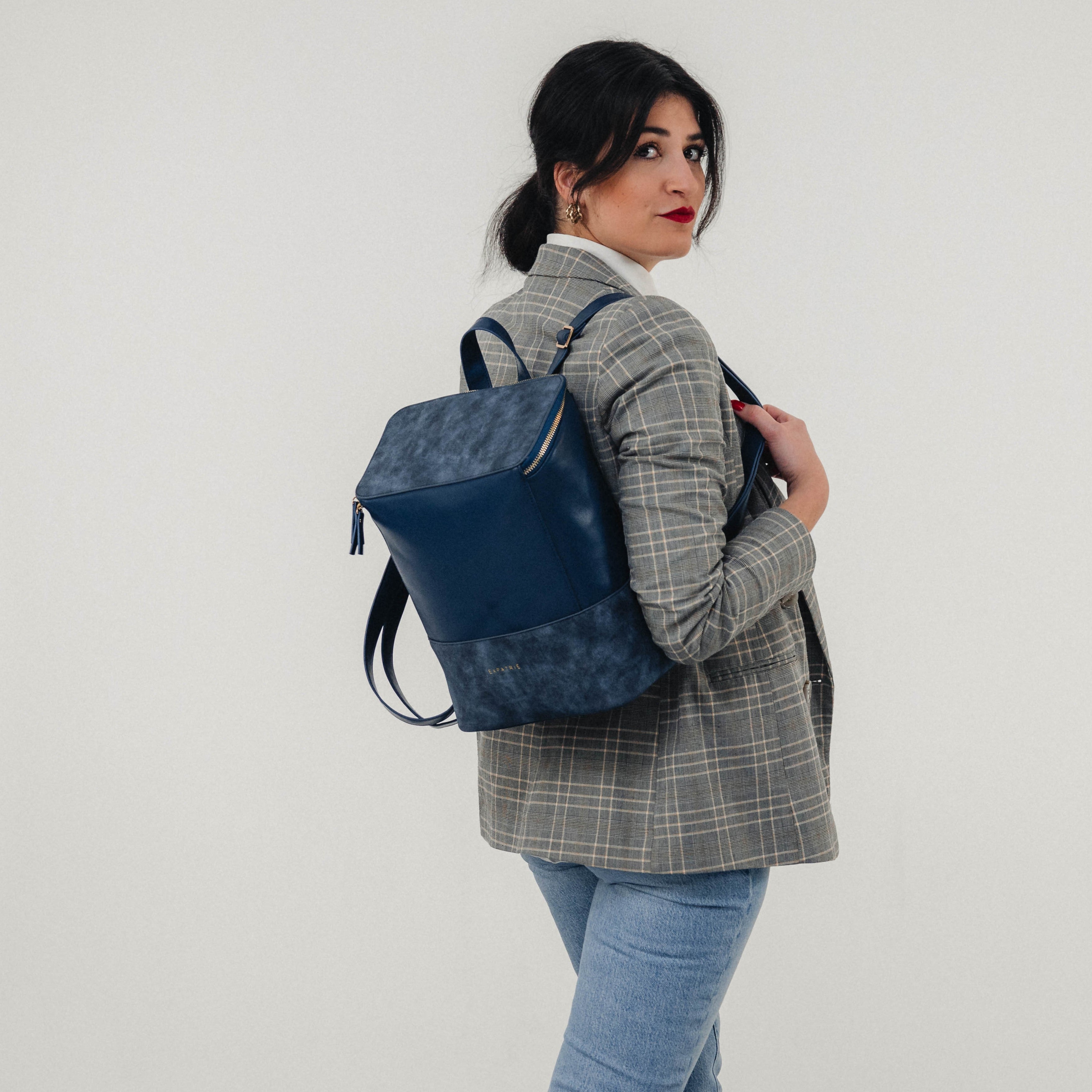 Frau mit grauem Karoblazer und Jeans trägt blauen Leder-Rucksack Malou auf dem Rücken
