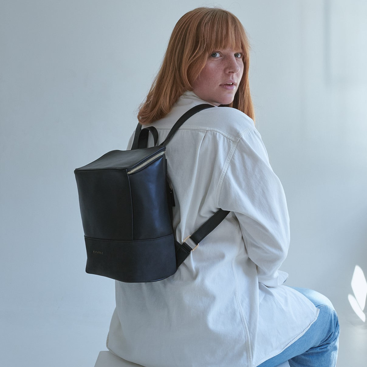 Frau mit roten Haaren trägt schwarzen Rucksack Malou aus Leder, sitzt und schaut zurück