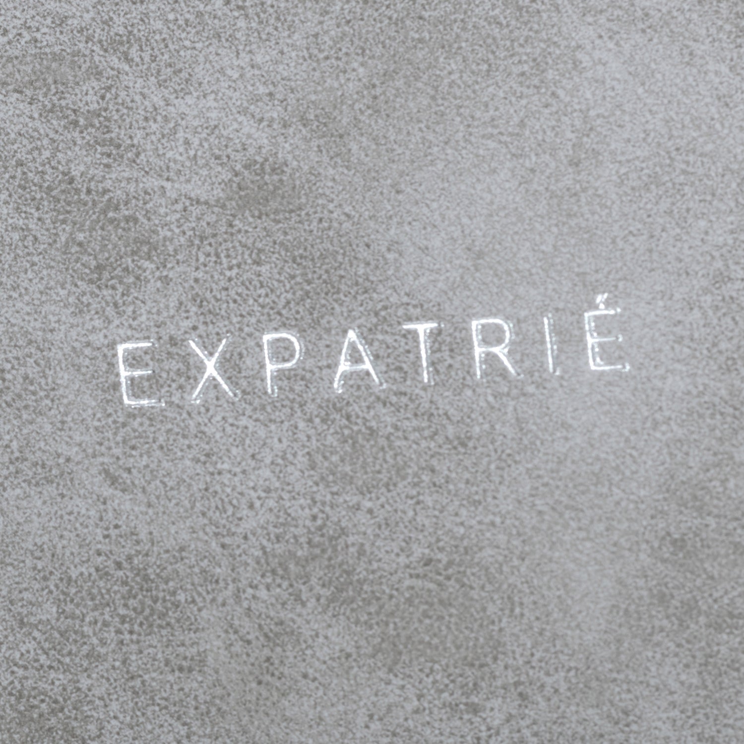 Nahe Aufnahme des grauen Kunstlederstoffs mit weißem 'EXPATRIÉ'-Logo