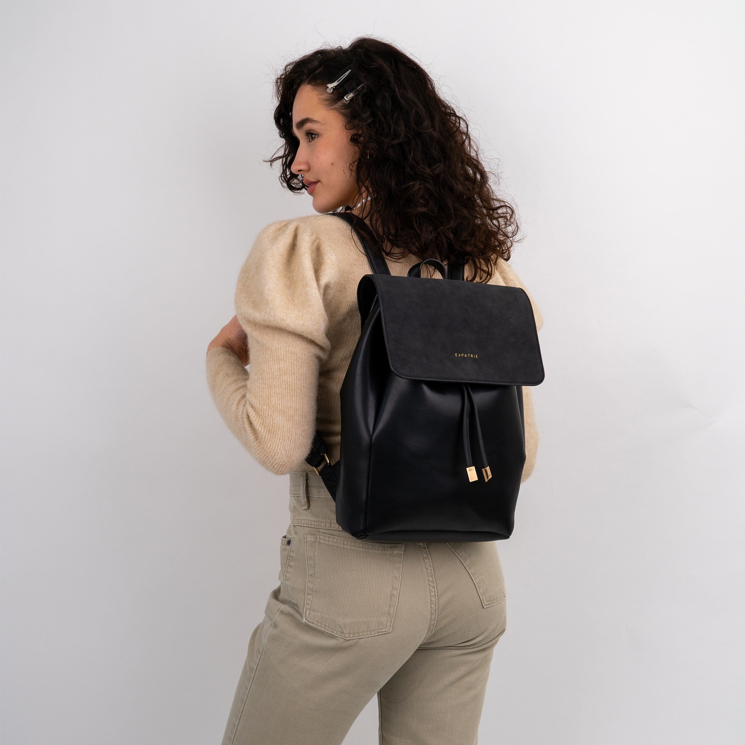 Frau mit beigem Pullover und hellen Hosen trägt schwarzen Kunstleder Rucksack 'Estelle' von Expatrié