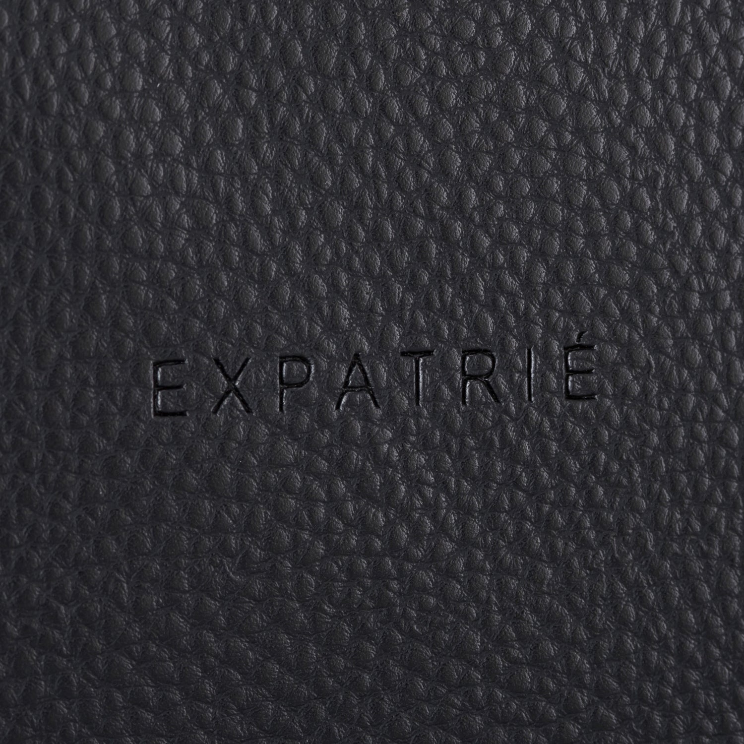Schwarze Lederoberfläche mit geprägtem Schriftzug 'EXPATRIÉ'