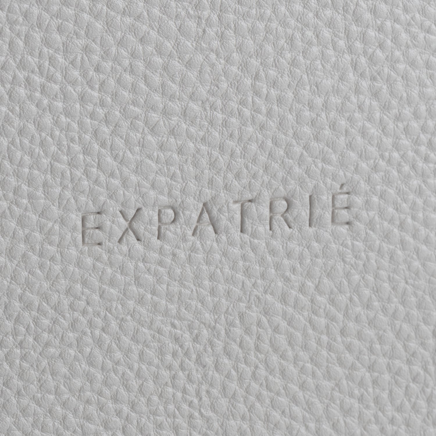 Nahaufnahme einer strukturierten Lederoberfläche mit dem geprägten Schriftzug 'EXPATRIÉ'