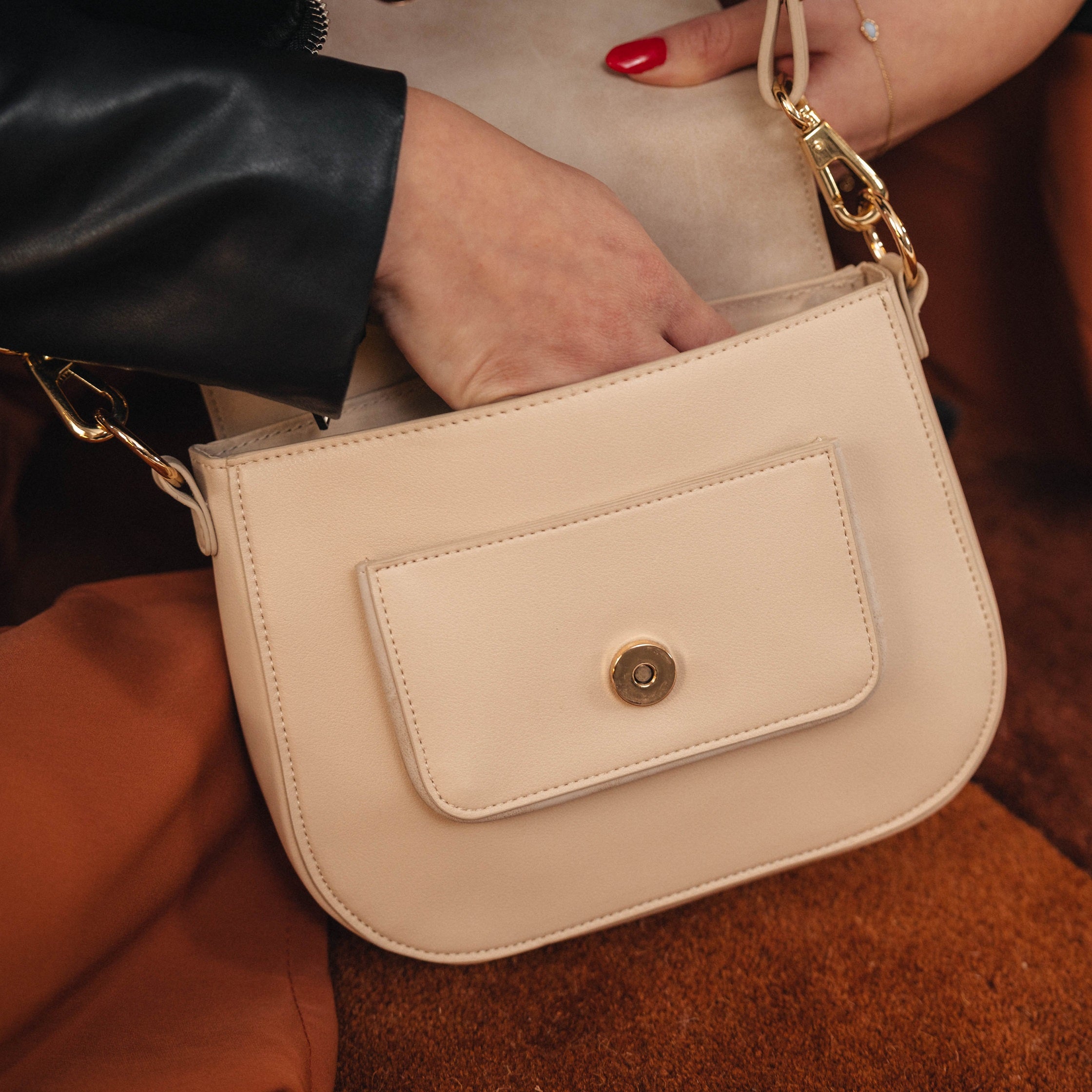 Beige Saddle Bag Louise Medium mit Vorderfach und goldfarbenen Details, Frau greift hinein