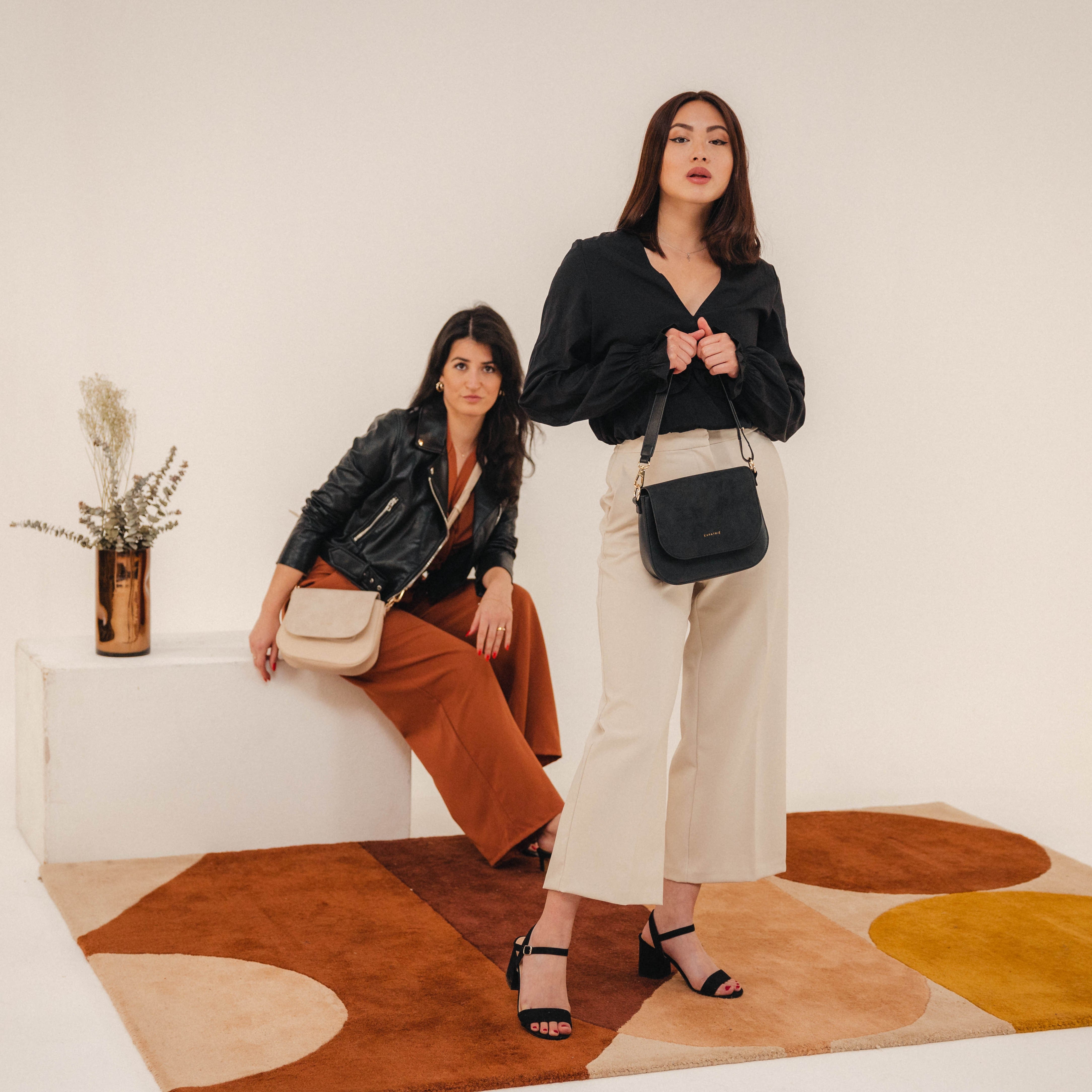 Zwei Frauen zeigen die Saddle Bag Louise Medium aus Leder, eine trägt eine schwarze Tasche, die andere eine beige.