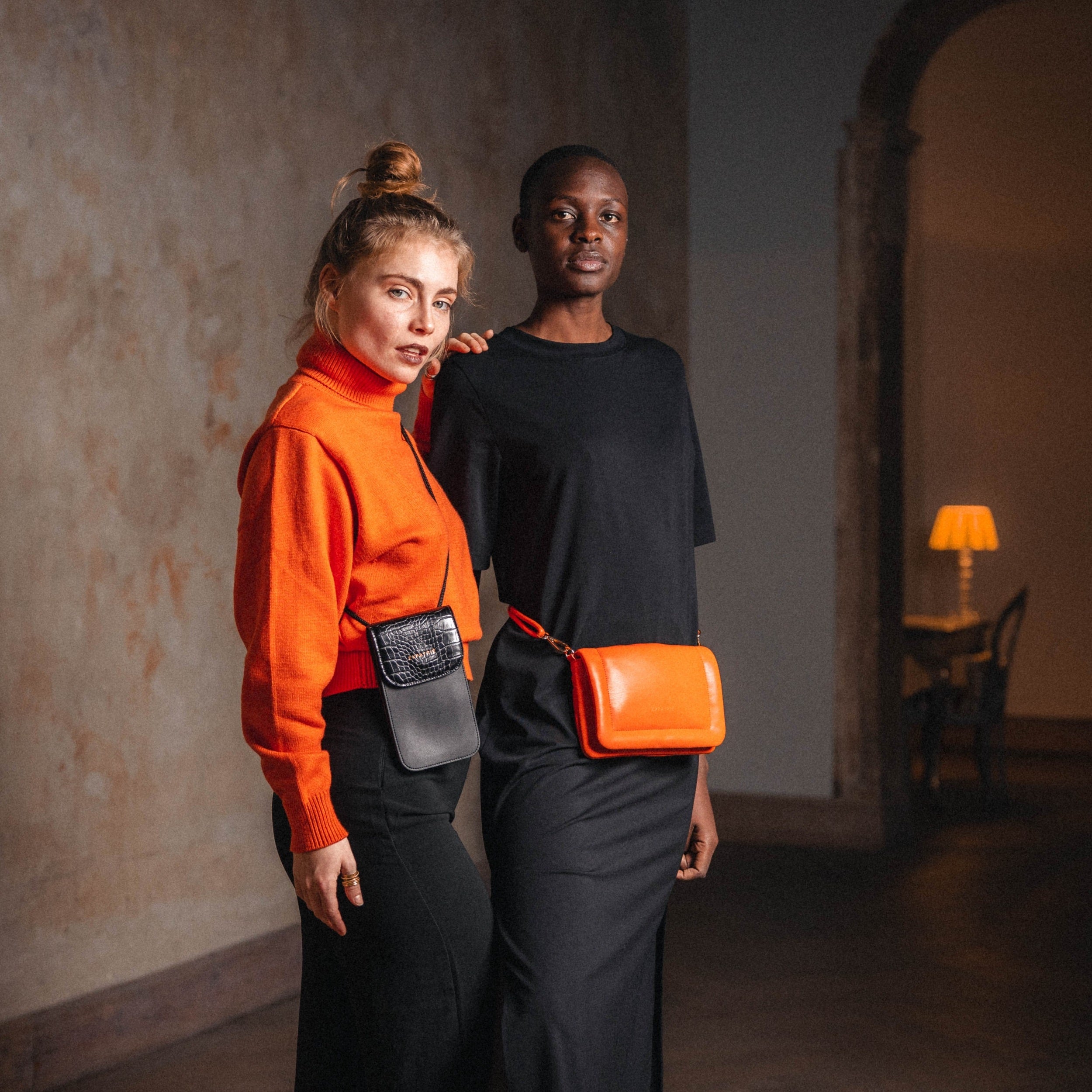 Zwei Frauen, eine mit oranger Umhängetasche Zoe Small aus Leder, die andere mit schwarzer Tasche mit Kroko-Prägung