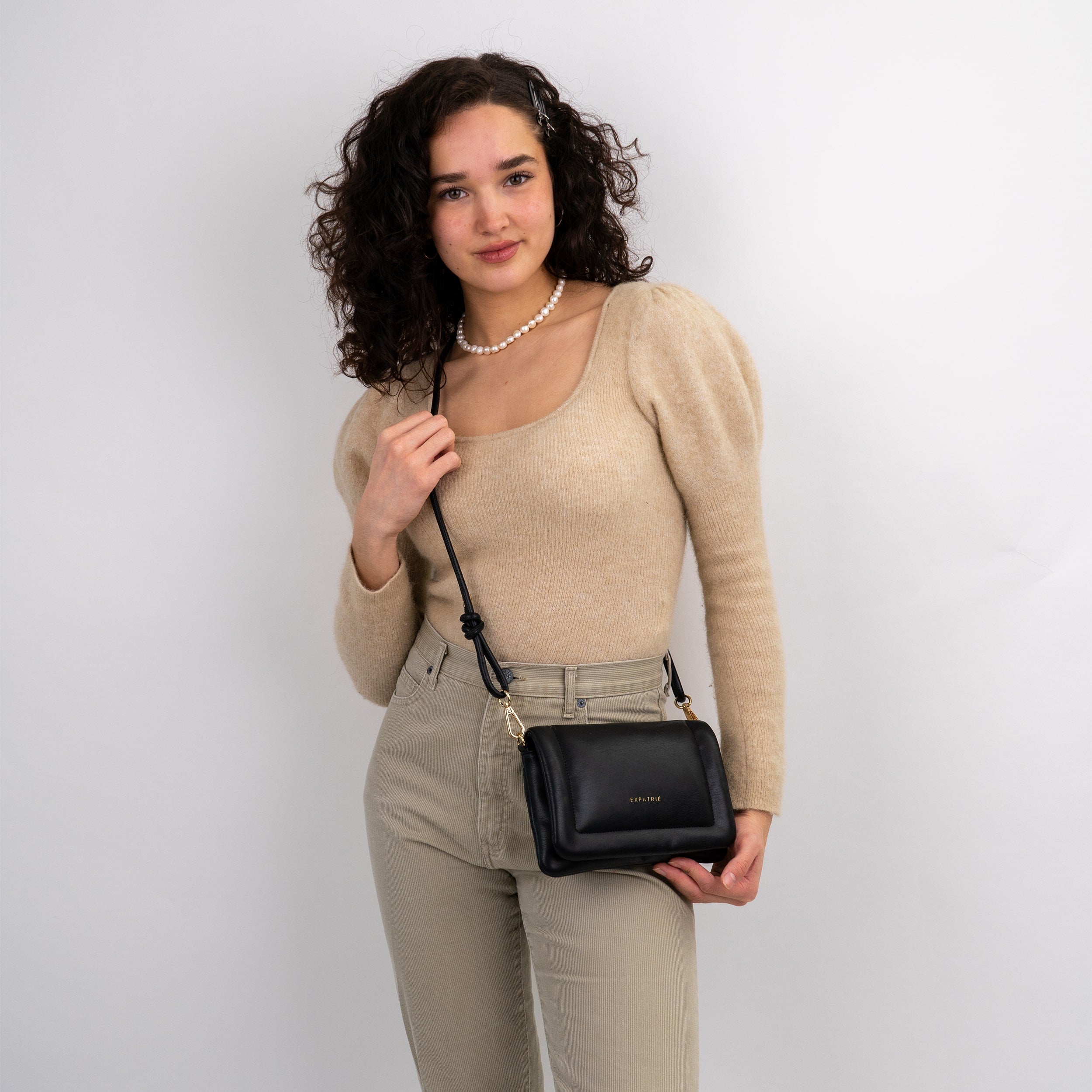 Frau trägt schwarze Umhängetasche 'Zoe Small' von Expatrié, beige Pullover mit Puffärmeln, helle Hose
