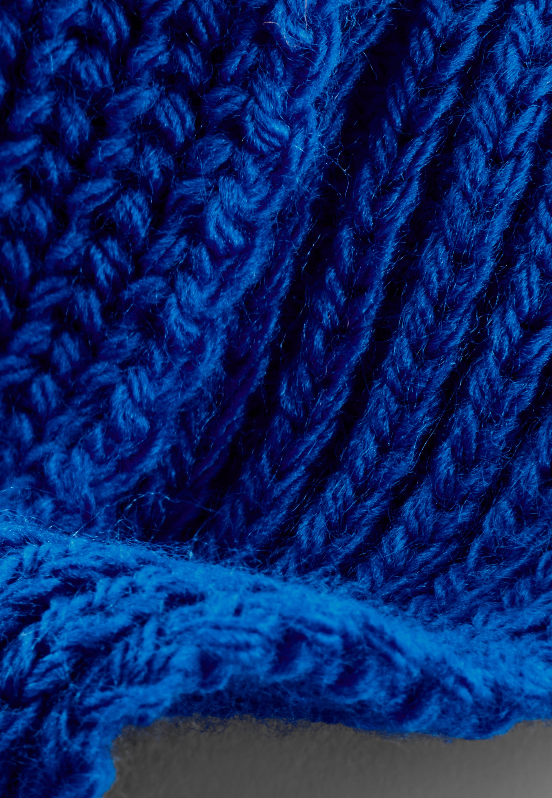 Nahaufnahme eines handgestrickten, royalblauen Schals mit unterschiedlichen Musterstrickarten