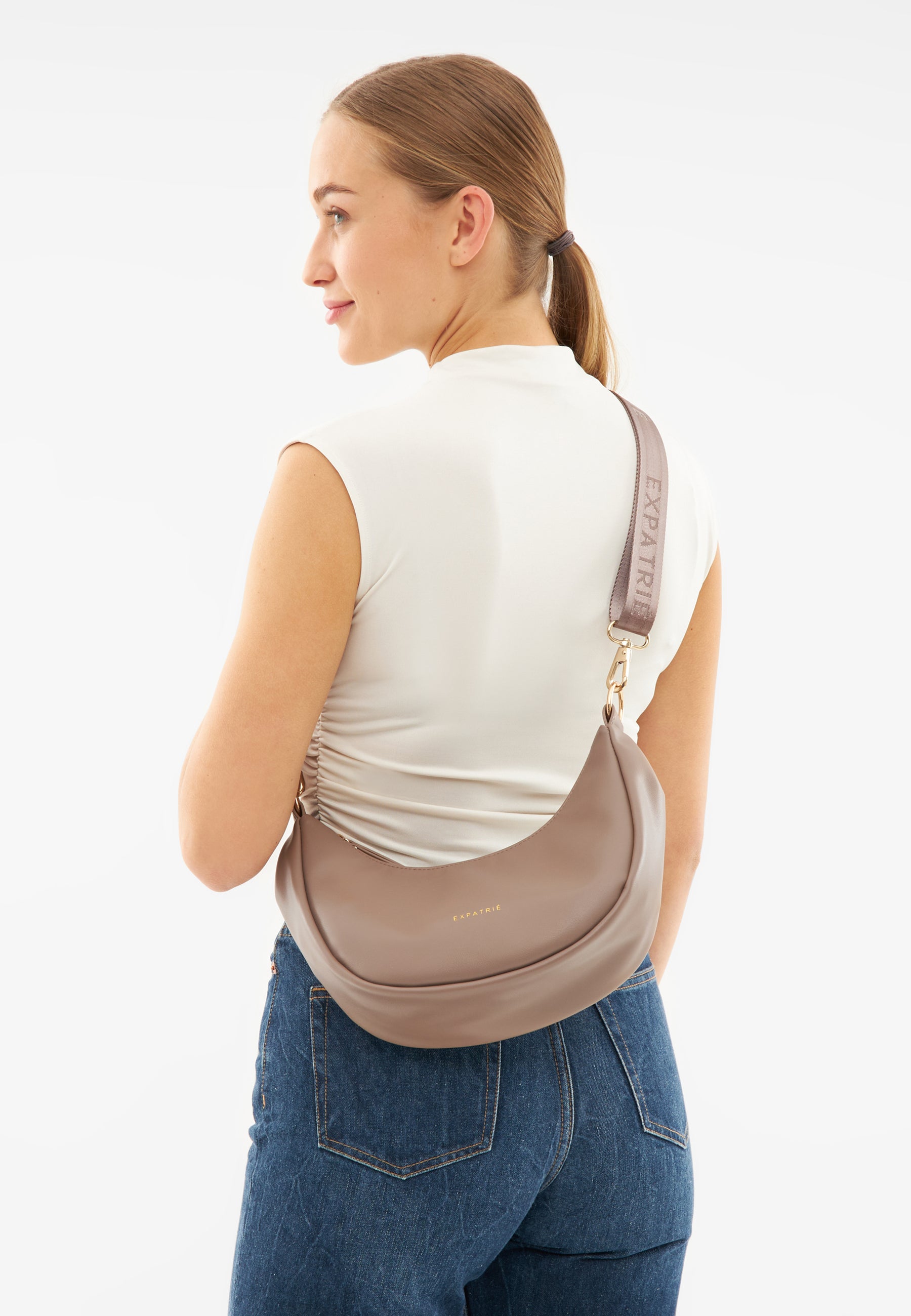Frau mit weißem ärmellosen Oberteil trägt braune LEA SMALL Half Moon Bag von Expatrié über der Schulter