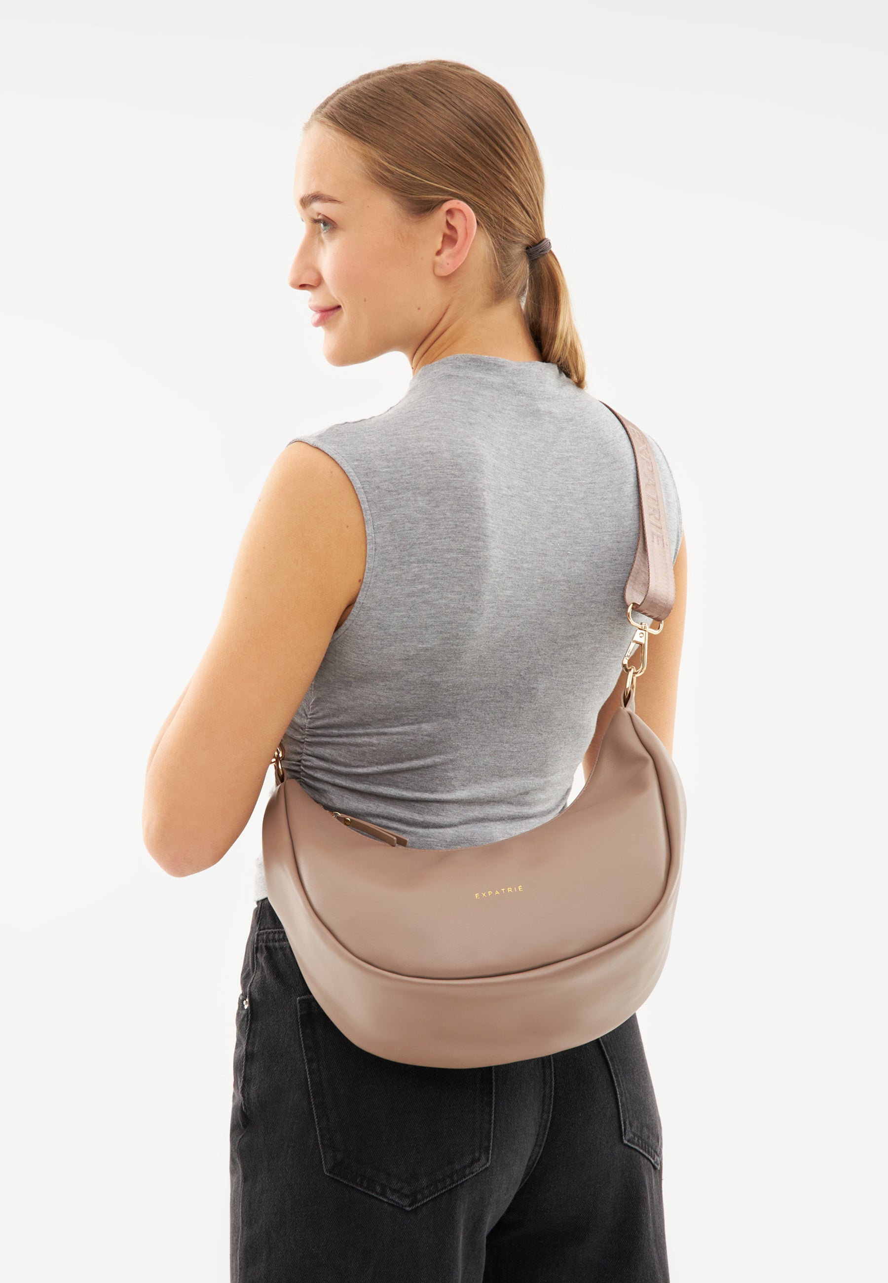Frau von hinten mit grauem ärmellosem Top und schwarzer Hose, trägt beige LEA MEDIUM Half Moon Bag über der Schulter
