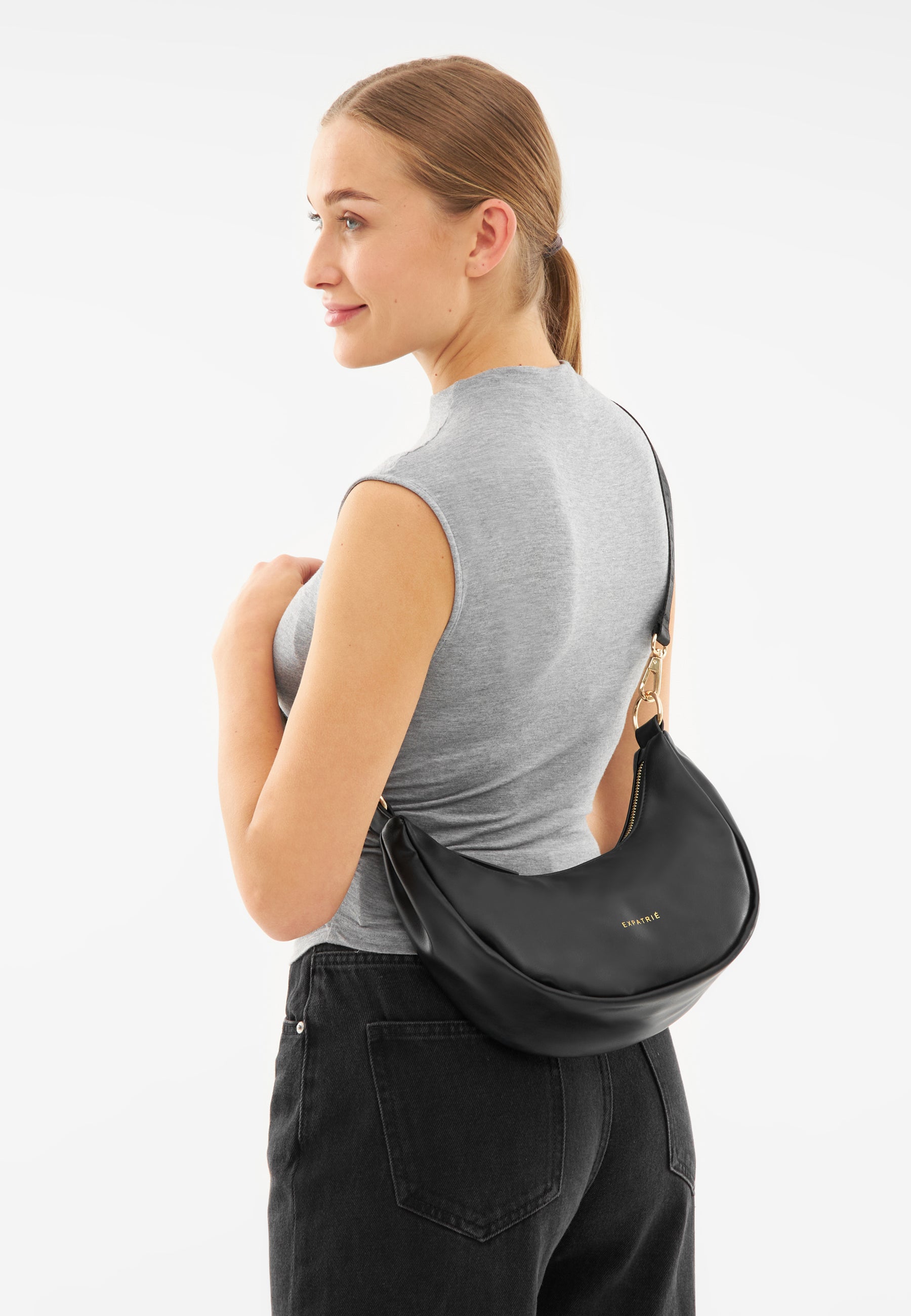 Frau mit grauem ärmellosem Top trägt schwarze LEA SMALL Half Moon Tasche über der Schulter