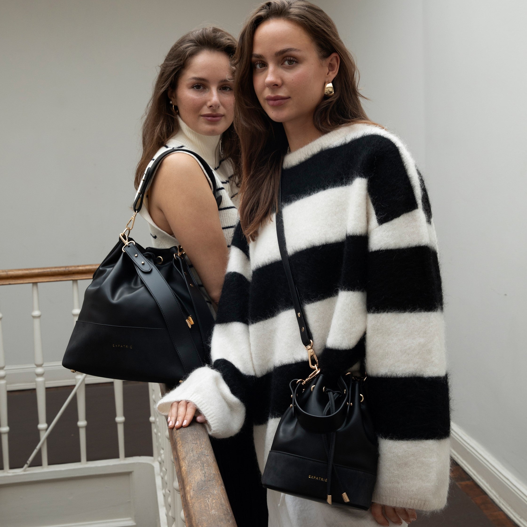 Zwei Frauen mit schwarzen Beuteltaschen Sarah Small aus Leder, eine trägt einen gestreiften Pullover, die andere ein ärmelloses Oberteil