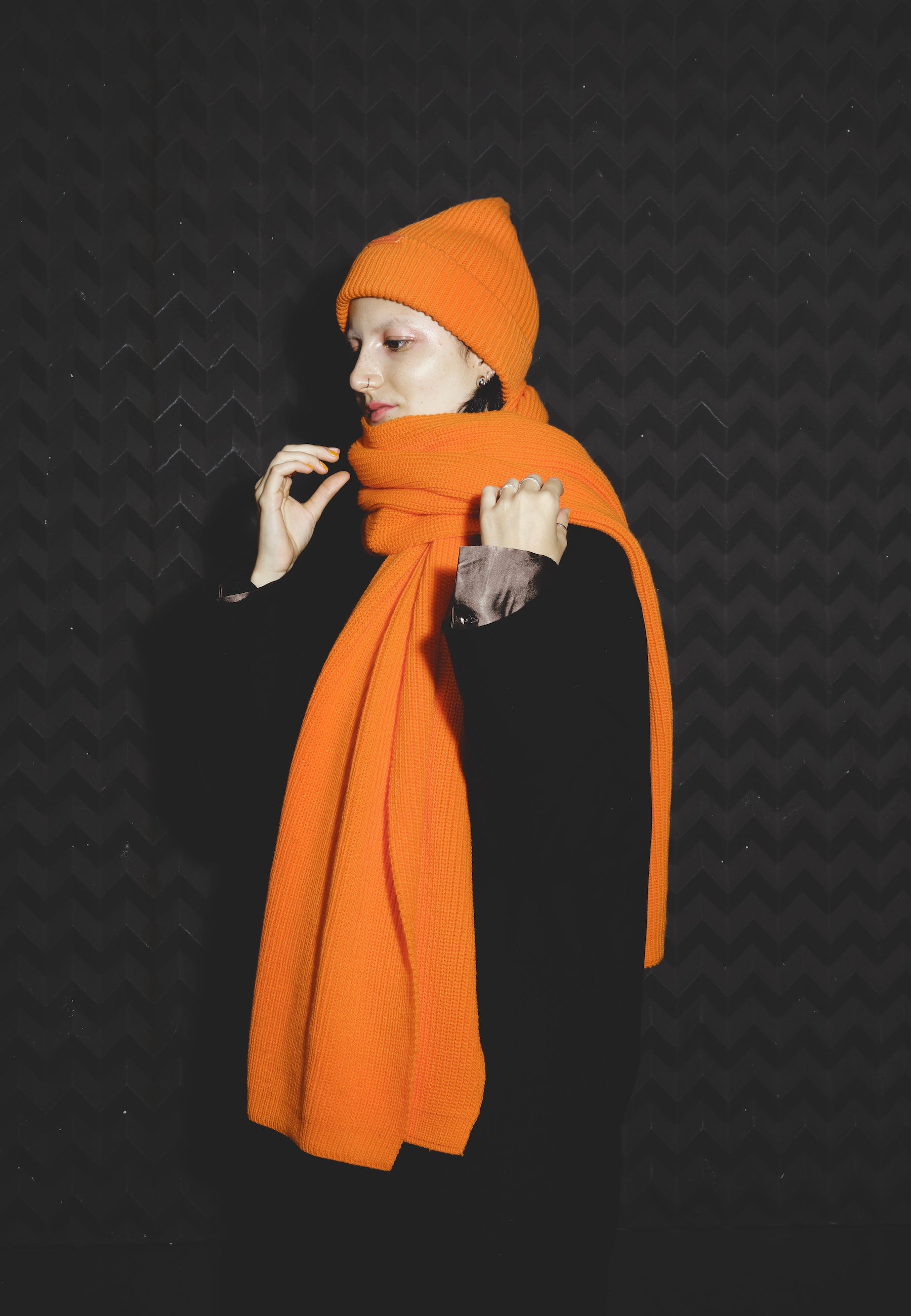 Frau trägt orange gestrickten Schal und Mütze vor dunklem Hintergrund