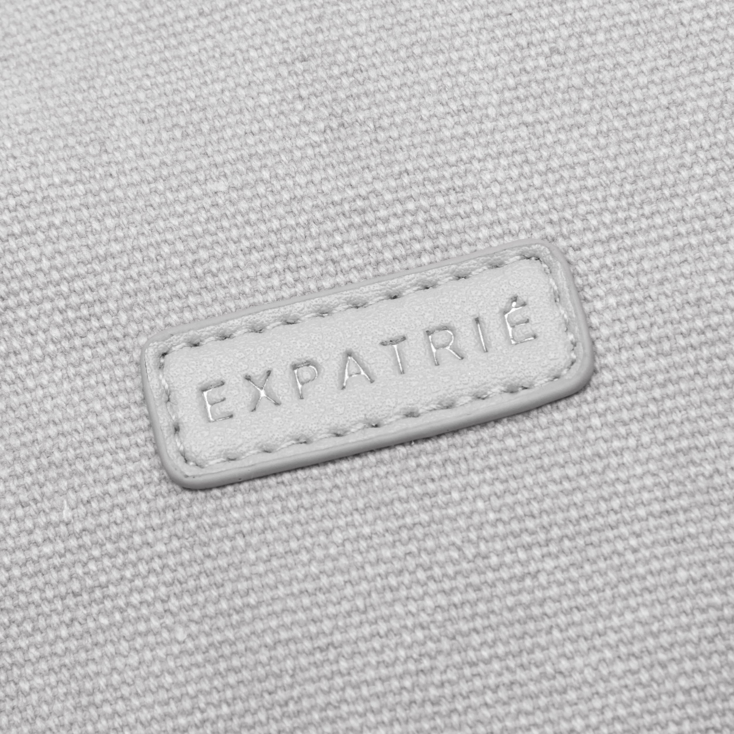 Nahaufnahme eines grauen Canvas-Materials mit aufgenähtem weißen Lederetikett 'EXPATRIÉ'