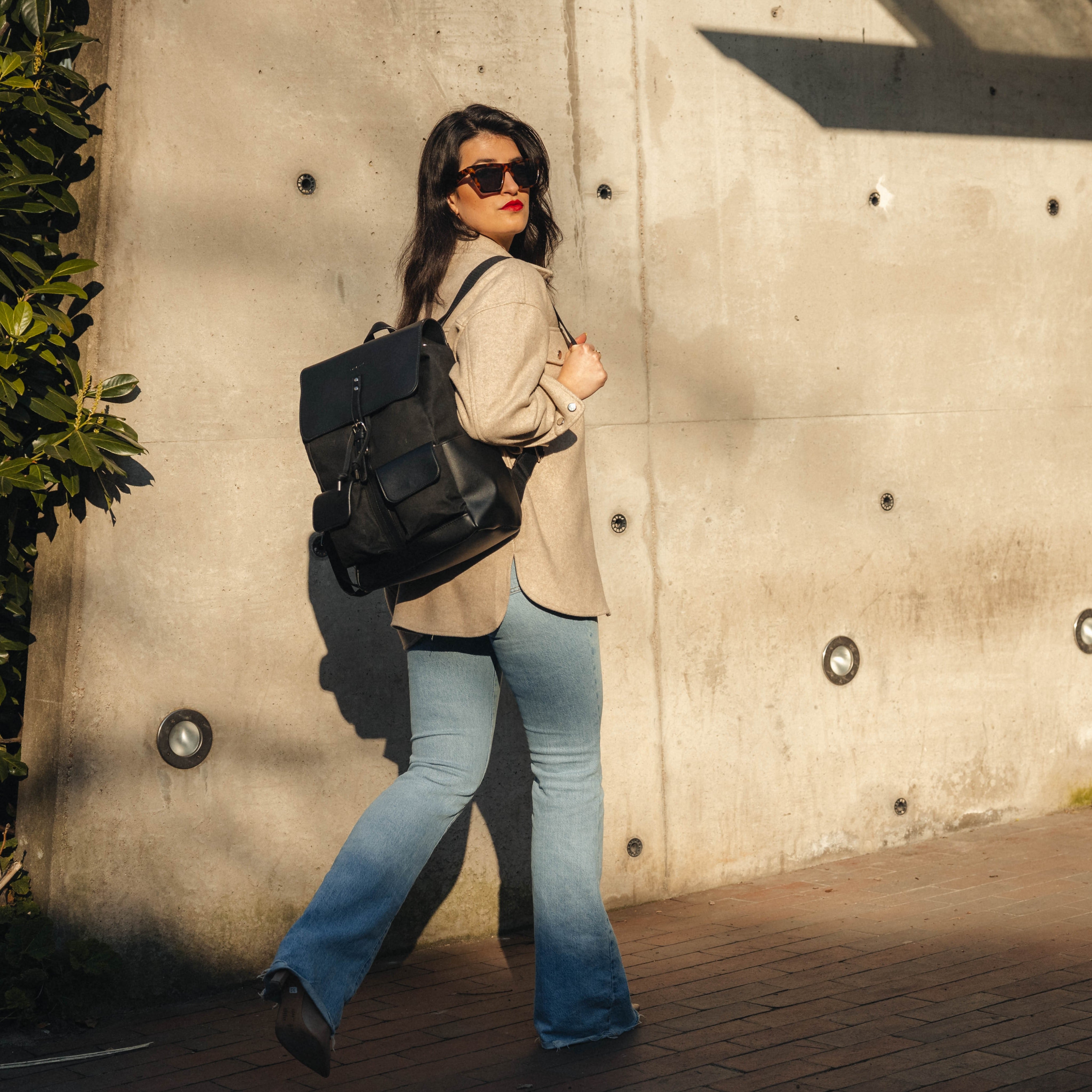 Frau mit schwarzem Rucksack Laurent aus Canvas und Leder, trägt beige Jacke und blaue Jeans